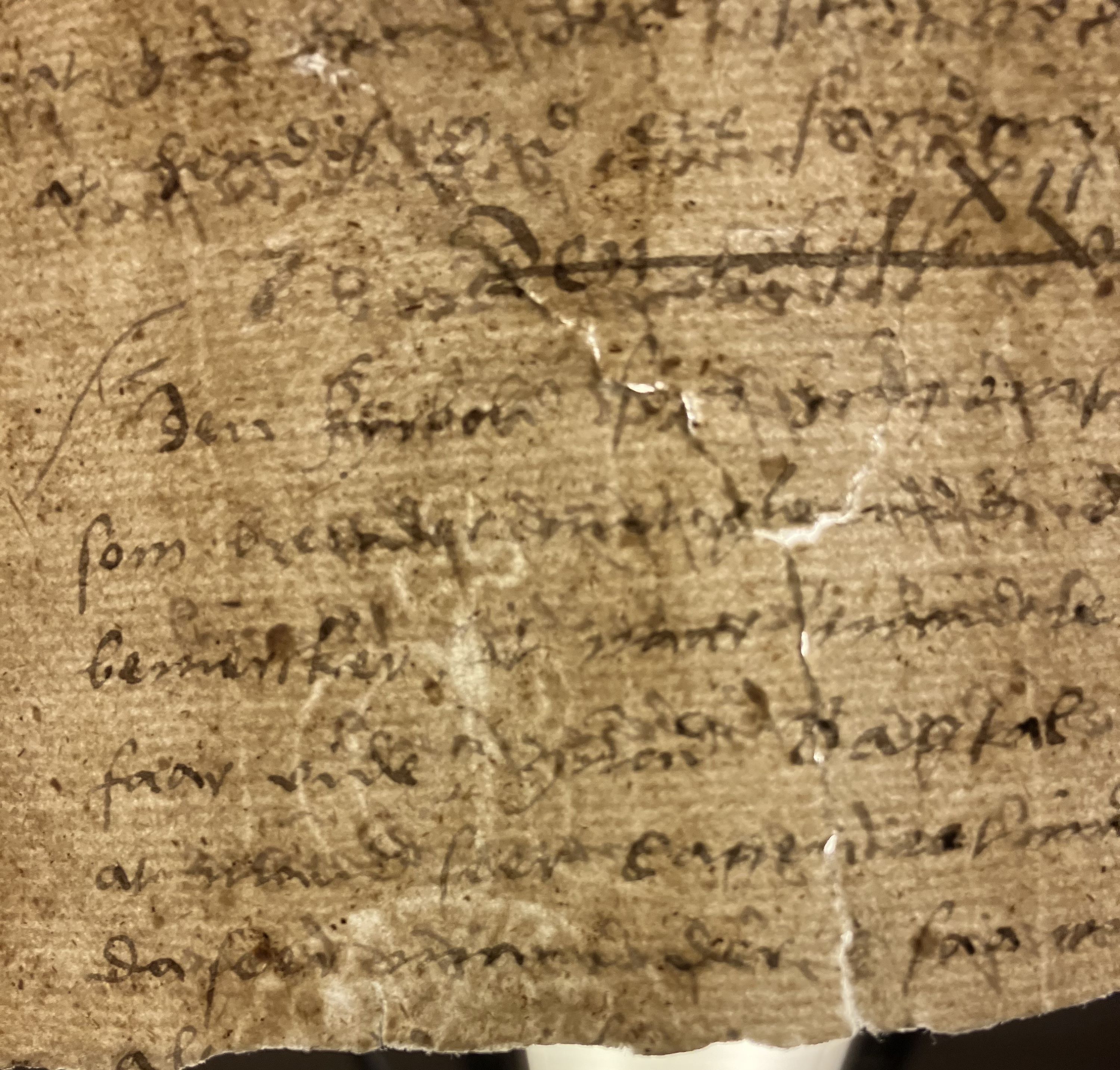 Närbild av ett gulnat och slitet pappersark där konturerna av ett vattenmärke framgår genom den handskrivna texten.